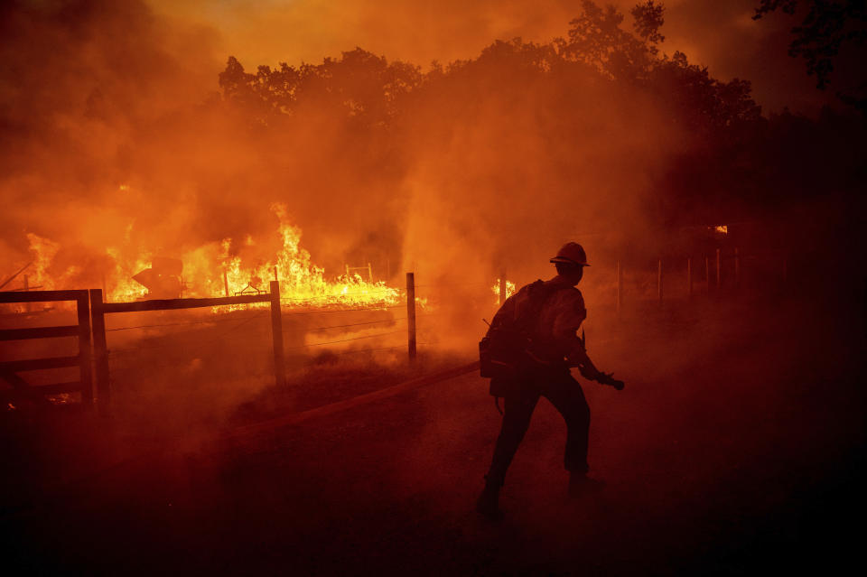 A firefighter runs to extinguish flames engulfing a structure.