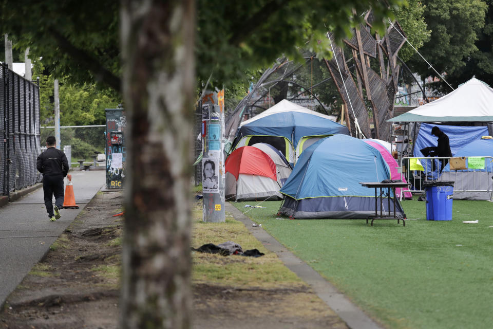 A jogger, left, runs past tents set-up on a play field in a city park Sunday, June 28, 2020, in Seattle, where several streets are blocked off in what has been named the Capitol Hill Occupied Protest zone. Seattle Mayor Jenny Durkan met with demonstrators Friday after some lay in the street or sat on barricades to thwart the city's effort to dismantle the protest zone that has drawn scorn from President Donald Trump and a lawsuit from nearby businesses. (AP Photo/Elaine Thompson)