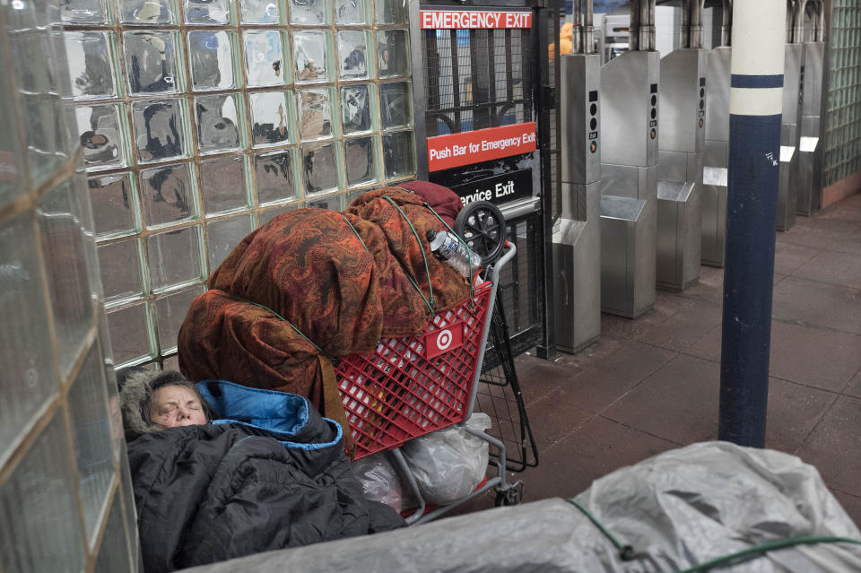 FILE - A homeless person sleeps under blankets next to a shopping cart of belongings in a New York subway station, on Jan. 9, 2018. New York Mayor Eric Adams is announcing a plan to boost safety in the city's sprawling subway network and try to stop homeless people from sleeping on trains or living in stations. (AP Photo/Mark Lennihan, File)