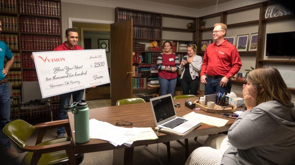 Jeray Jarreau (seated), Bless Your Heart founder and director, is surprised by a donation presented by Peter Louviere (left), CFO of REV Broadband/Vision Communications, and Josh Descant (right), CEO of REV Broadband/Vision Communications.