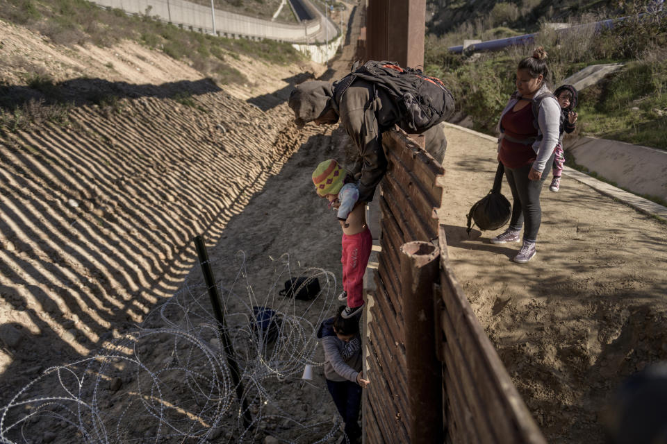 FILE - In this Saturday, Dec. 29, 2018, file photo, a man passes a Mexican migrant baby to her mother after they jump the border fence to get to the U.S. side to San Diego, from Tijuana, Mexico. (AP Photo/Daniel Ochoa de Olza, File)