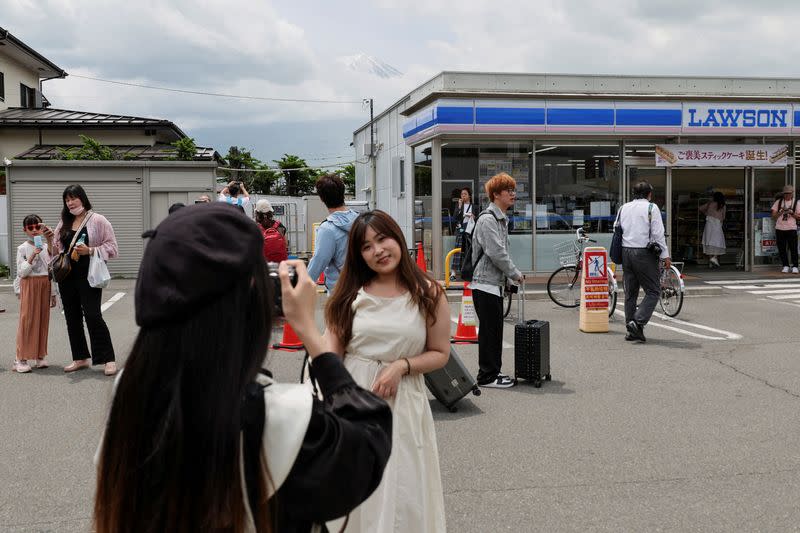 Tourists take photos of Mount Fuji appearing over a convenience store in Fujikawaguchiko town
