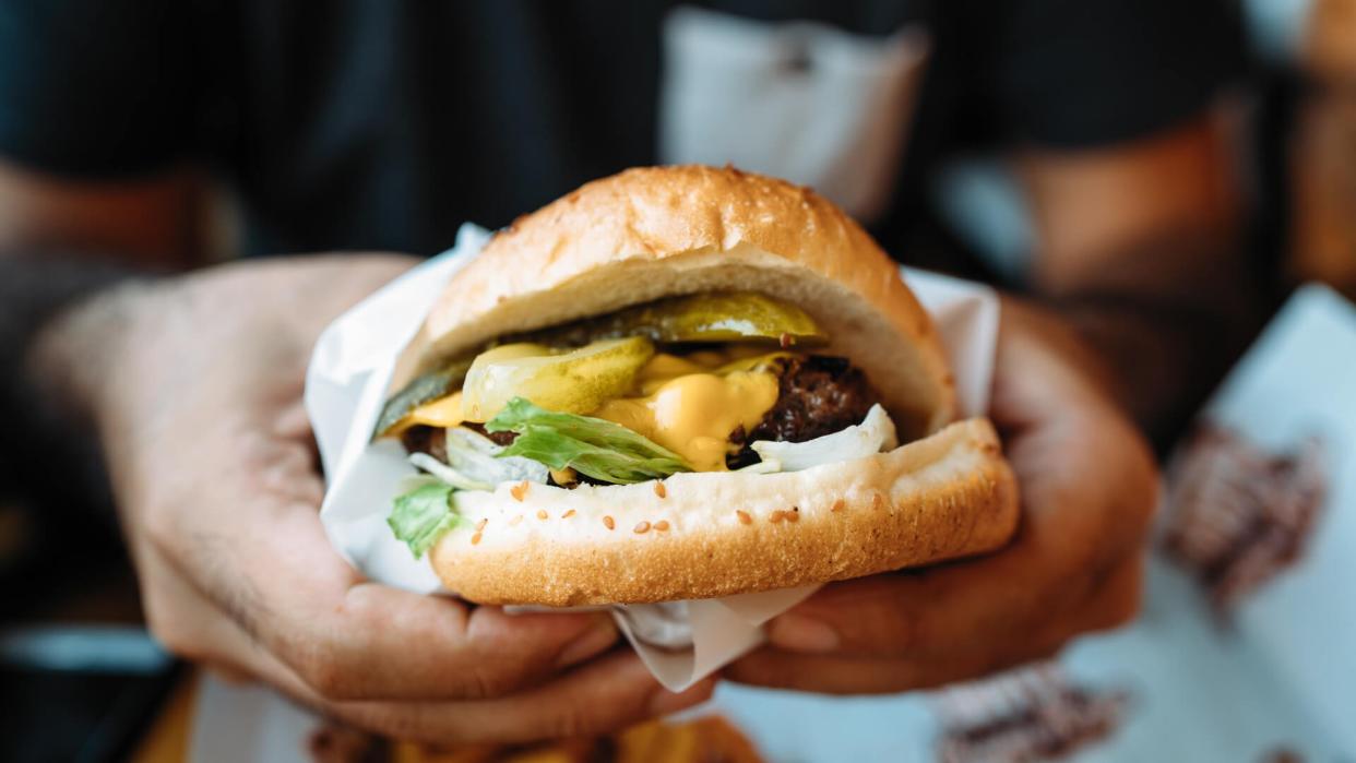 Man holds cheeseburger with hands.