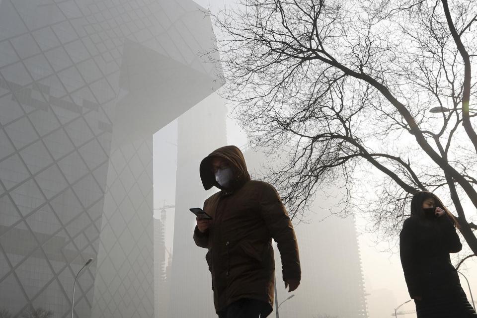 People wearing protection masks walk near the iconic headquarters of China's state broadcaster Central China Television (CCTV) at the Central Business District in Beijing as the capital of China is blanked by heavy smog on Tuesday, Jan. 3, 2017. China's Ministry of Environment says an unspecified number of companies have violated measures meant to reduce smog as the country deals with a phase of particularly noxious pollution. Beijing has been on "orange alert" the second highest pollution alert level since Friday. The alert was originally due to end on Sunday but authorities have extended it a further three days. (AP Photo/Andy Wong)