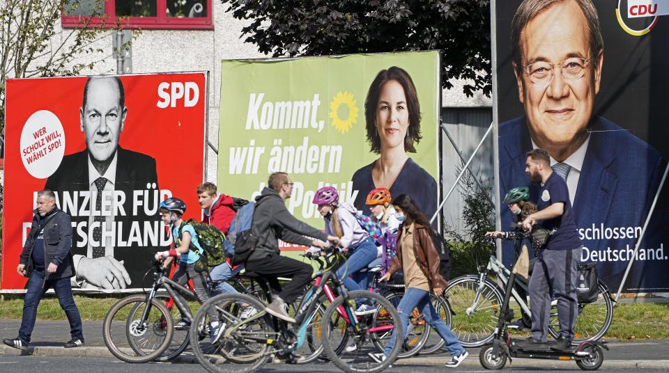 People walk and drive past election posters of the three chancellor candidates, from right, Armin Laschet, Christian Democratic Union (CDU), Annalena Baerbock, German Green party (Die Gruenen) and Olaf Scholz, Social Democratic Party (SPD), at a street in Gelsenkirchen, Germany, Thursday, Sept. 23, 2021 three days before the General election on Sunday, Sept. 26, 2021. (AP Photo/Martin Meissner)