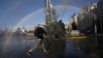 An anti-government protester runs from police water cannons, on the day Chileans vote in a referendum to decide whether the country should replace its 40-year-old constitution, written during the dictatorship of Gen. Augusto Pinochet, in Santiago, Chile, Sunday, Oct. 25, 2020. (AP Photo/Luis Hidalgo)