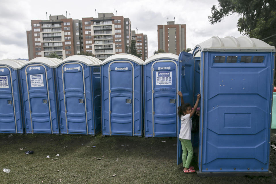 A girl enters a portable toilet at a camp set up for homeless Venezuelan migrants in Bogota, Colombia, Wednesday, Nov. 21, 2018. The camp, built by the city's social welfare agency to accommodate migrants who had previously been living in tents made of plastic sheets and scrap materials outside the city's bus terminal, houses more than 400 people. (AP Photo/Ivan Valencia)
