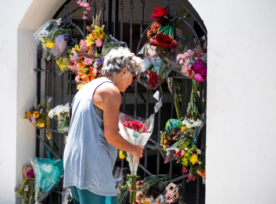 A passerby puts flowers on a gate covered in flowers outside of Mother Emanuel AME Church on the anniversary of the shooting seven years ago, in Charleston, S.C., Friday, June 17, 2022. 