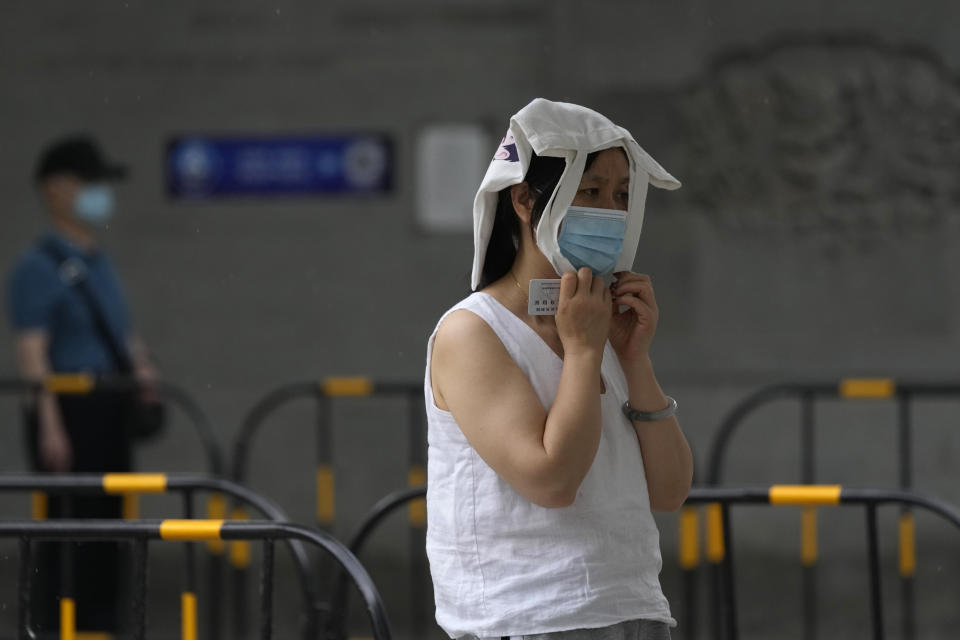 A resident covers her head as it starts to rain at a mass COVID test site, Sunday, May 29, 2022, in Beijing. (AP Photo/Ng Han Guan)