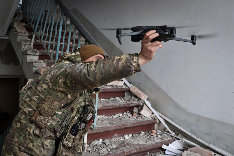 A Ukrainian solider in combat gear holds a drone up in a rubble-filled stairwell in Bakhmut