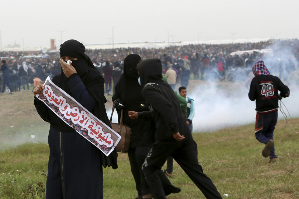 Protesters run to cover from teargas fired by Israeli troops near fence of Gaza Strip border with Israel, marking first anniversary of Gaza border protests east of Gaza City, Saturday, March 30, 2019. Arabic reads that " Millionth of the land and return". Tens of thousands of Palestinians on Saturday gathered at rallying points near the Israeli border to mark the first anniversary of weekly protests in the Gaza Strip, as Israeli troops fired tear gas and opened fire at small crowds of activists who approached the border fence. (AP Photo/Adel Hana)