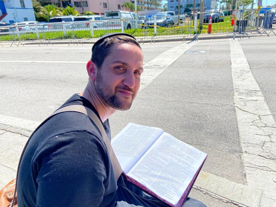 Michael Benmeleh from Aventura, sits on a sidewalk Sunday, July 4, 2021, on Harding Avenue in Surfside, reading the Talmud for the victims of the Champlain Towers South building collapse.