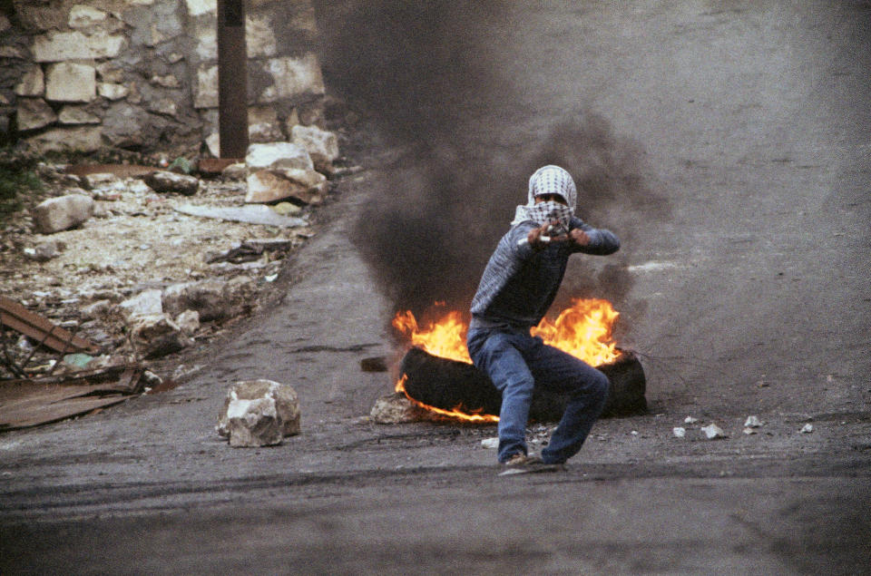 FILE - In this Jan. 14, 1988, file photo taken by Max Nash, a Palestinian teenager aims a slingshot in front of a blazing tire at photographers and Israeli soldiers in the Israel-occupied West Bank town of Nablus. Nash, who covered the conflicts in Southeast Asia and the Middle East and helped nurture a new generation of female photojournalists during more than 40 years with The Associated Press, died Friday, Sept. 28, 2018, after collapsing at home. He was 77. (AP Photo/Max Nash, File)