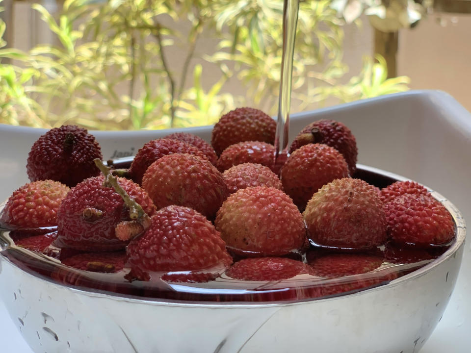 Water is being poured over red lychees in a white bowl