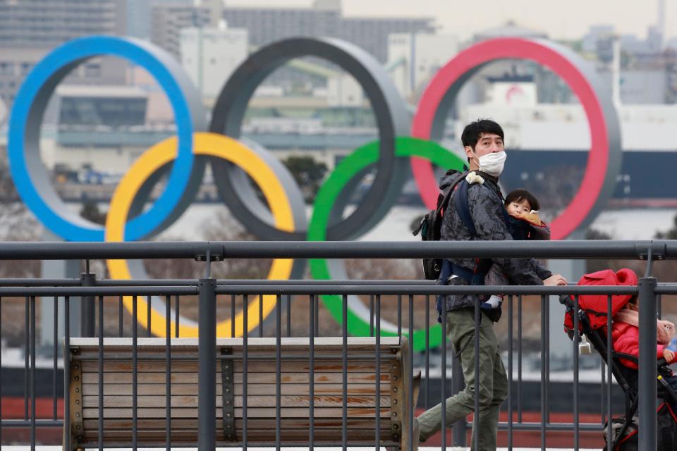 People wearing face masks to protect against the spread of the coronavirus walk on the Odaiba waterfront as Olympic rings are seen in the background in Tokyo, Tuesday, Jan. 26, 2021. (AP Photo/Koji Sasahara)