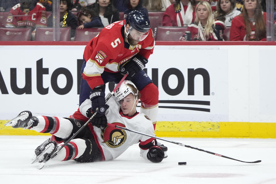 Florida Panthers defenseman Aaron Ekblad (5) and Ottawa Senators left wing Parker Kelly (27) battle for the puck during the first period of an NHL hockey game, Tuesday, Feb. 20, 2024, in Sunrise, Fla. (AP Photo/Wilfredo Lee)