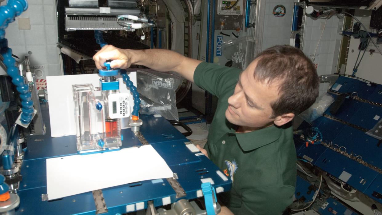  A man with short hair holds medical equipment inside of a cramped laboratory. 