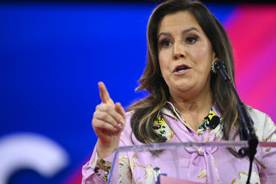 Elise speaking at a podium with a microphone, gesturing with her index finger raised