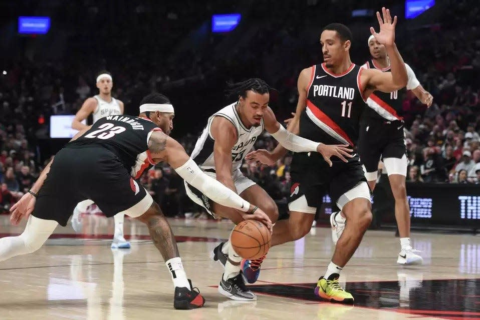 Portland Trail Blazers forward Ish Wainright, left, pokes the ball away from San Antonio Spurs guard Tre Jones, while Blazers guard Malcolm Brogdon, right, defends during the first half of an NBA basketball game in Portland, Ore., Thursday, Dec. 28, 2023.