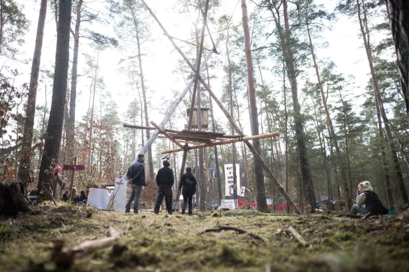 People stand in front of a camp organized by the "Stop Tesla" initiative in a pine forest near the Tesla Gigafactory Berlin-Brandenburg. The permit for the camp expires this Friday at midnight and is expected to be evacuated next weekend. Sebastian Gollnow/dpa