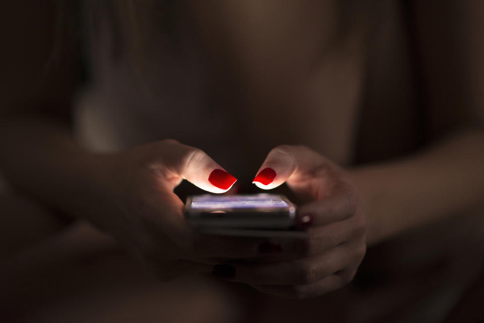 Close-up of a person with red nail polish texting on a smartphone in a dimly lit setting