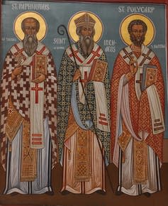 Three saints stand in an icon image, with golden halos around their heads.