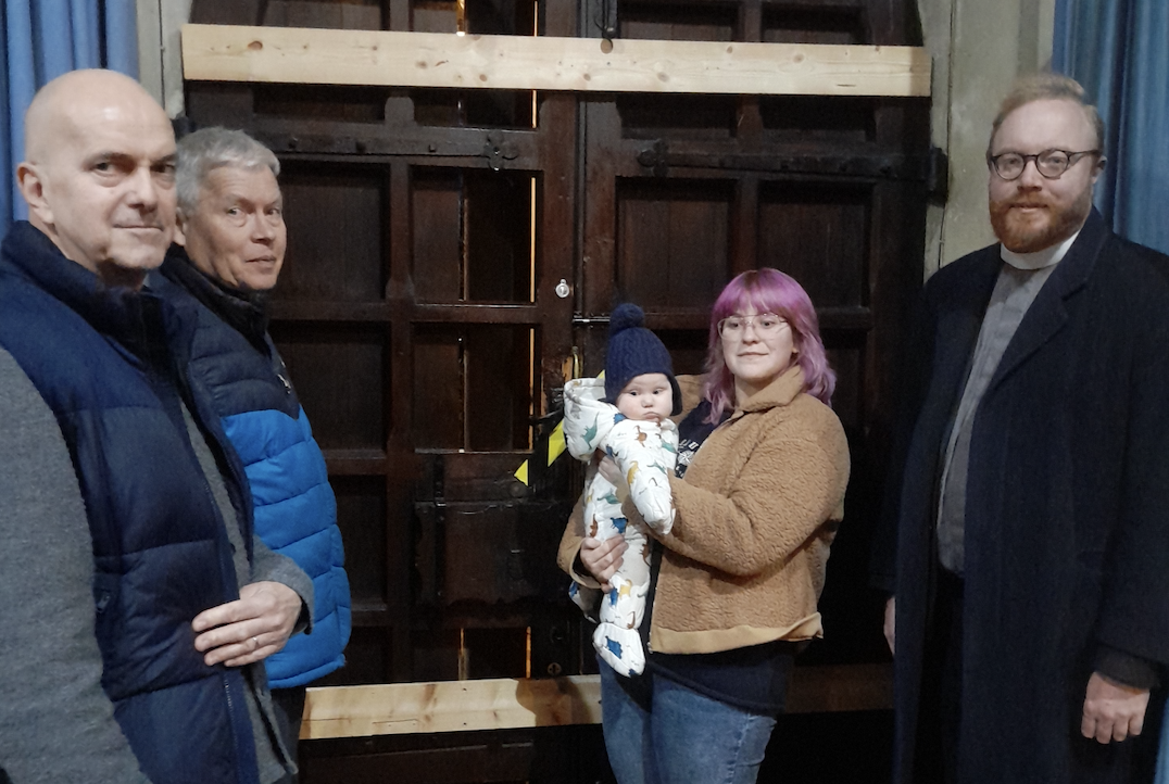 The rector of Wanstead, Fr James Gilder, right, with some of his parishioners in front of the door that was damaged by thieves to gain entry to the church. (Wanstead Parish)