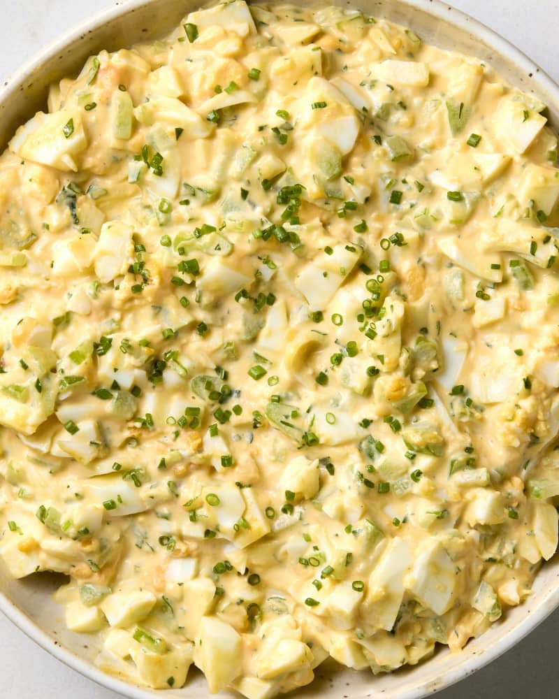 overhead shot of egg salad in a white bowl, topped with chives.