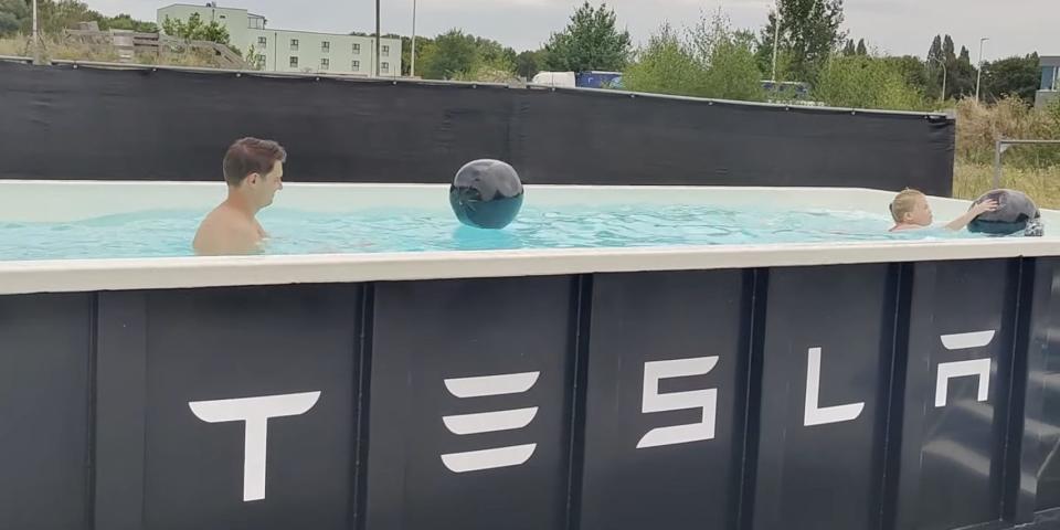 a man and a little girl swim in a black metal pool that has tesla written on the front of it