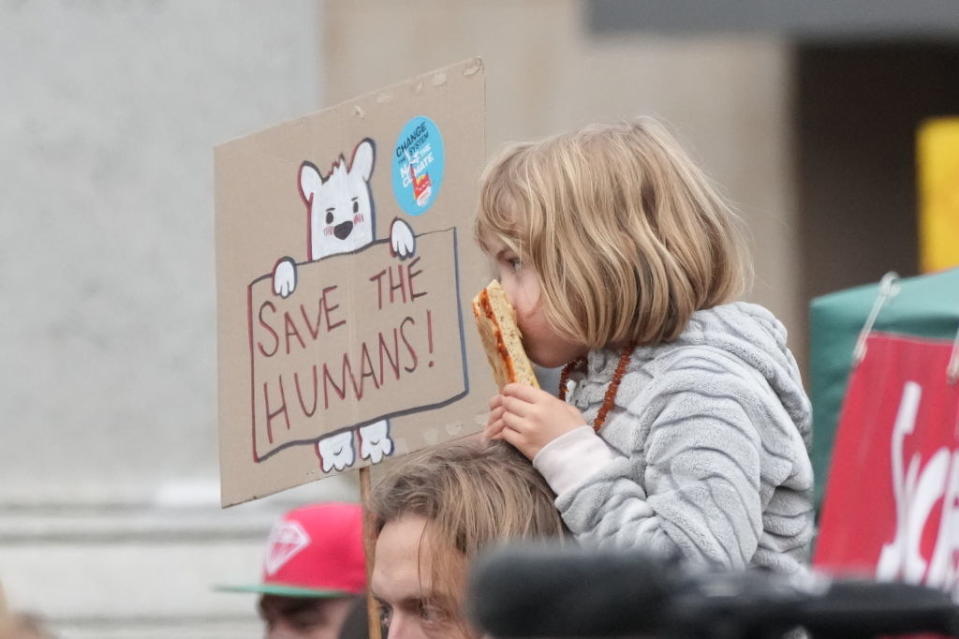 A young girl at the protest sitting on the shoulders of an adult with a sign nearby that says 'Save the Humans'