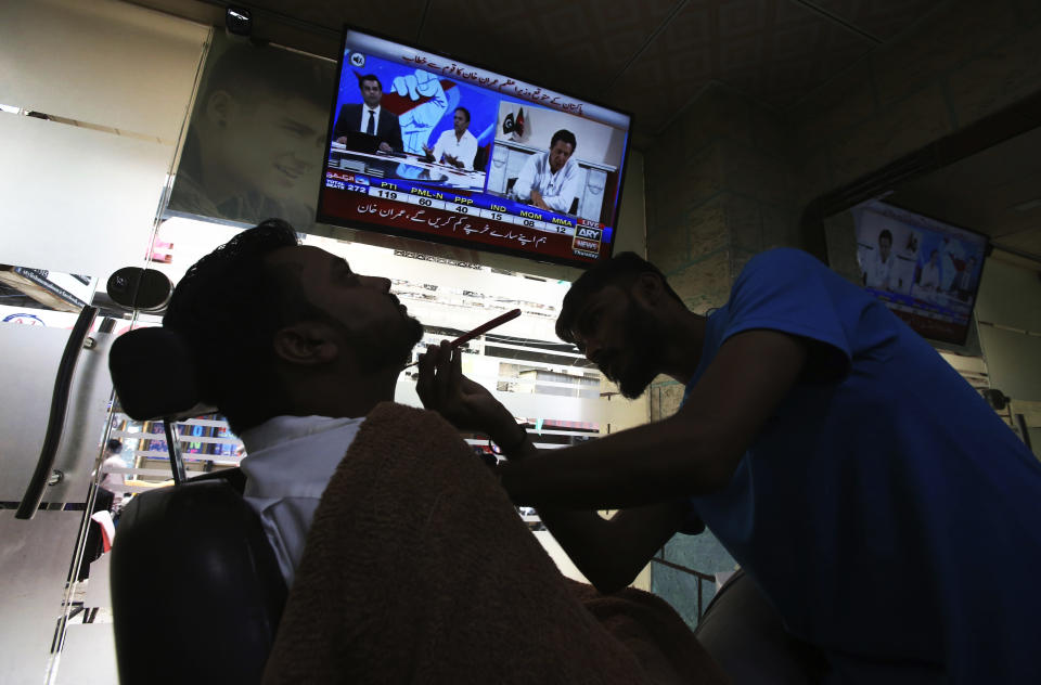 A customer listens the speech of Pakistani politician Imran Khan, chief of Pakistan Tehreek-e-Insaf party, telecasting on news channels at a barber shop in Karachi, Pakistan, Thursday, July 26, 2018. Khan declared victory Thursday for his party in the country's general elections, promising a "new" Pakistan following a vote that was marred by allegations of fraud and militant violence. (AP Photo/Fareed Khan)