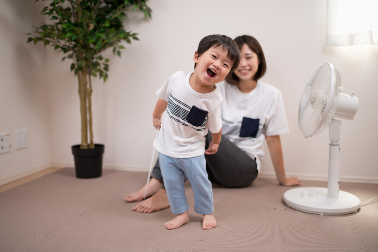 A mother sitting down, and a child standing in front of a fan, illustrating the story of a household saving electricity by using a fan