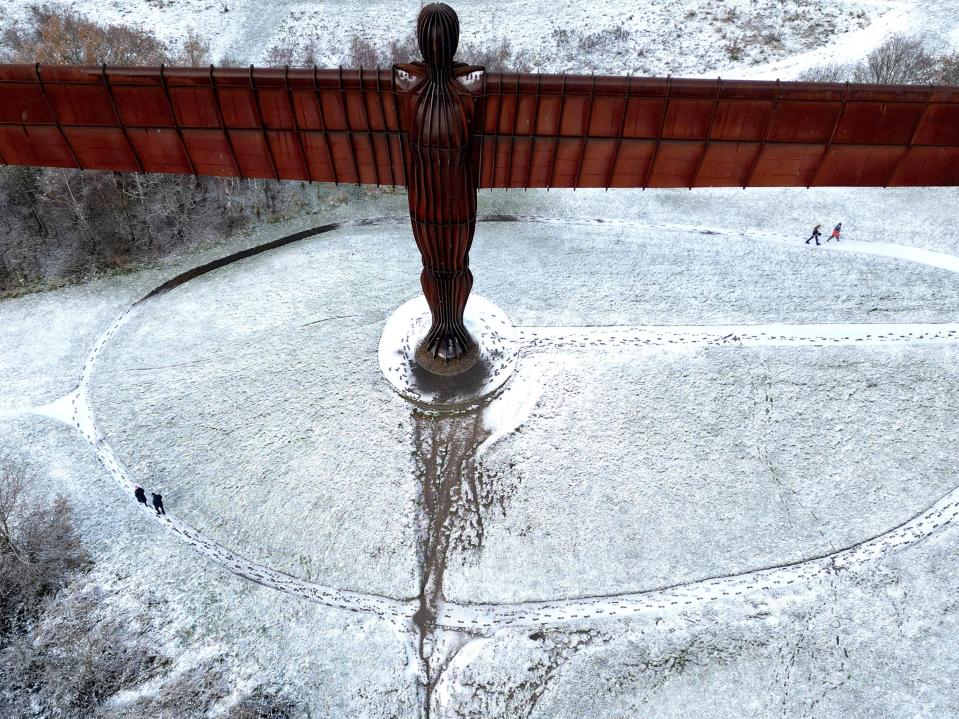 People walk next to Antony Gormley’s Angel of the North as snow continues to fall in Gateshead (REUTERS)