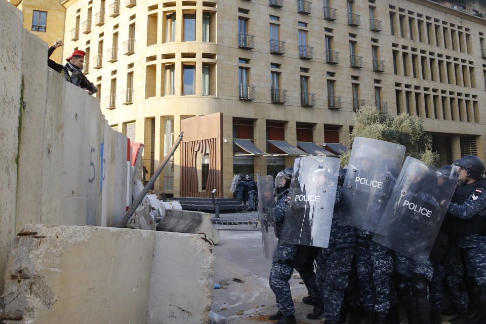 An anti-government demonstrator throws stones toward riot police on a road leading to the parliament building, during a protest against a parliament session to vote of confidence for the new government, in downtown Beirut, Lebanon, Tuesday, Feb. 11, 2020. (AP Photo/Bilal Hussein)