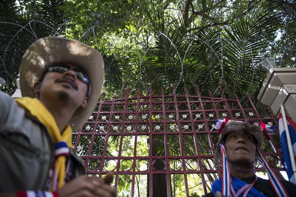 Anti-government protesters of People's Democratic Reform Committee (PDRC) stand under a fence topped with barbed wire outside the Royal Thai Police headquarters in the Pathumwan district, Wednesday, Jan. 15, 2014, in Bangkok, Thailand. Gunshots rang out in the heart of Thailand's capital overnight in an apparent attack on anti-government protesters early Wednesday that wounded at least two people and ratcheted up tensions in Thailand's deepening political crisis. (AP Photo/John Minchillo)