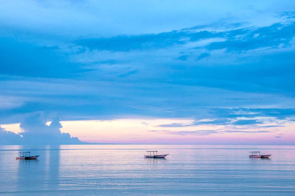 Endless ocean blue water with three fishing boats at sunset, very calming