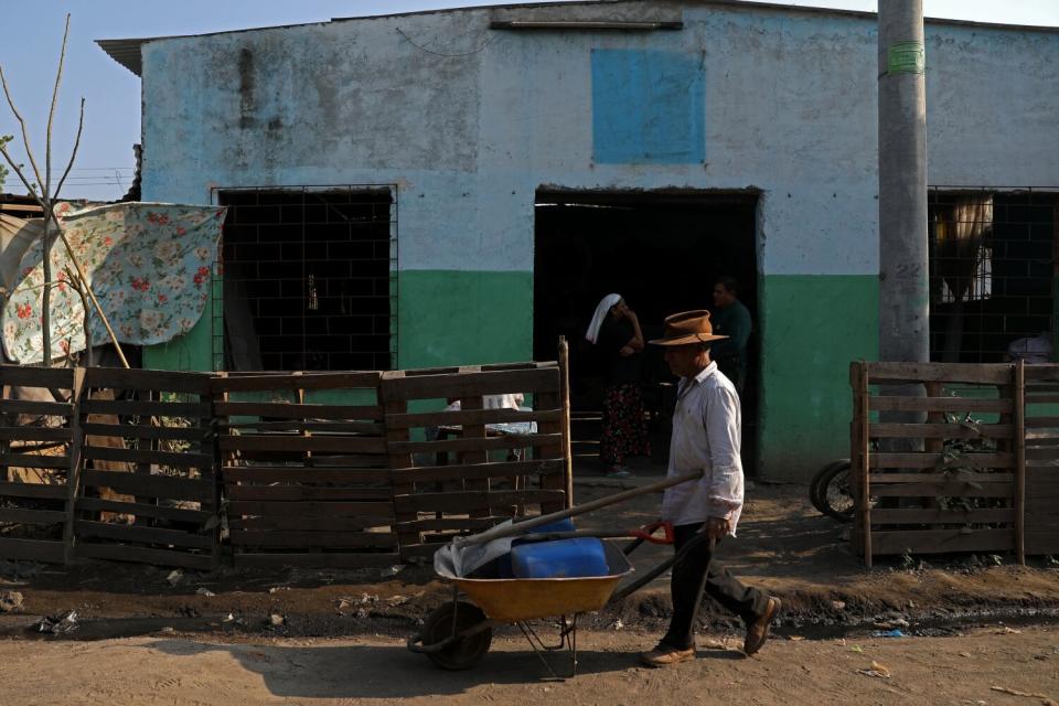 A man pushes a wheelbarrow past a rustic building painted in blue, white and green