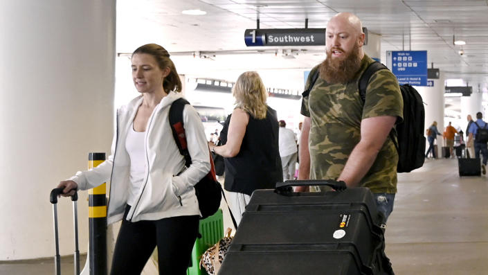 Two people, not wearing masks, wheel suitcases through an airport.