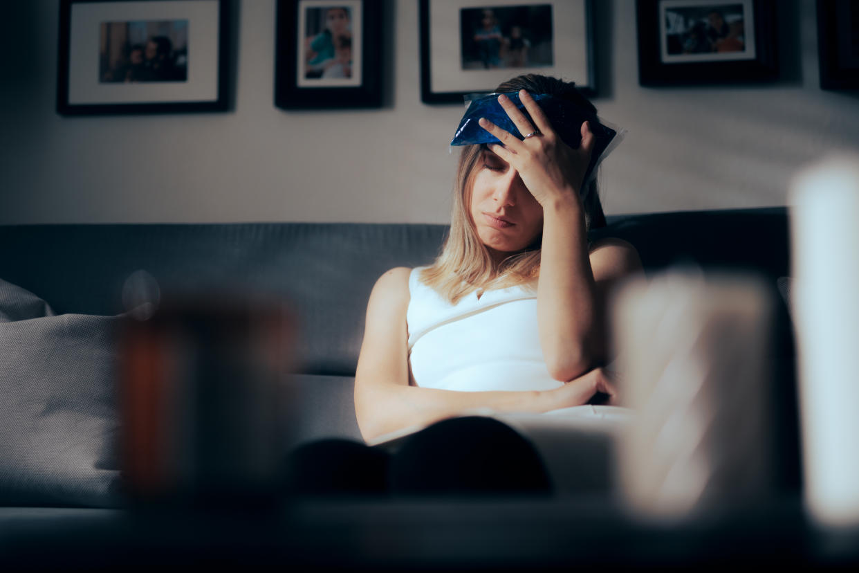 A woman on a couch using a migraine cap.