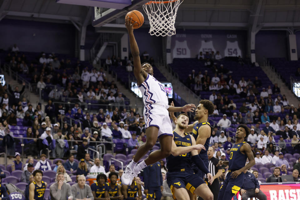 TCU guard Shahada Wells (13) leaps to the basket for a shot over West Virginia guard Erik Stevenson, center bottom, in the first half of an NCAA college basketball game, Tuesday, Jan. 31, 2023, in Fort Worth, Texas. (AP Photo/Ron Jenkins)