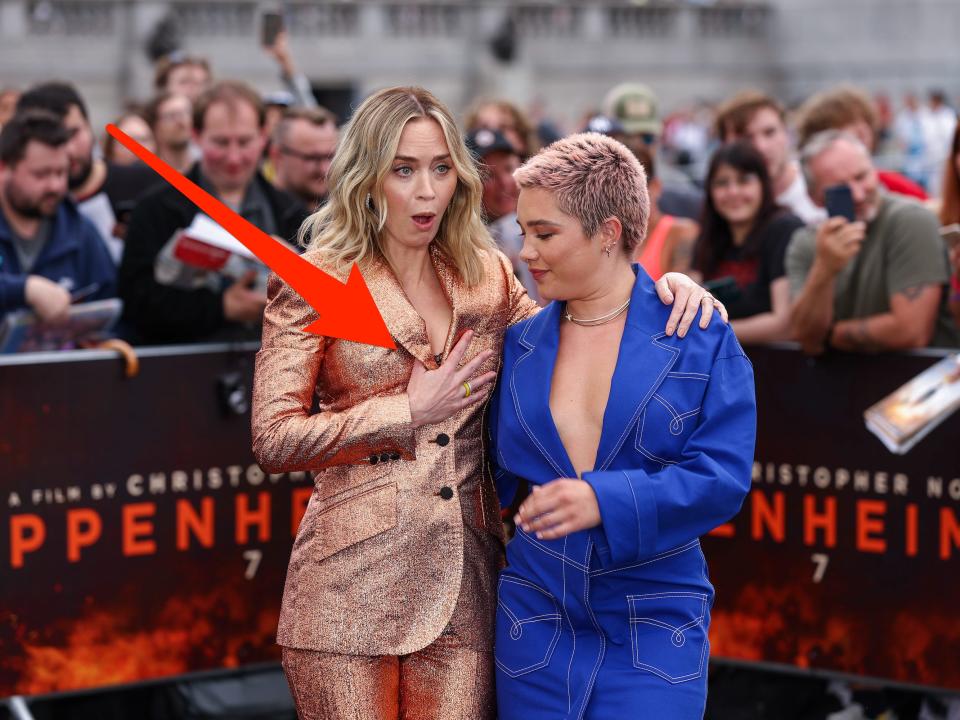 Emily Blunt holds the front of her blazer while posing for photos while Florence Pugh looks on. A red arrow, digitally inserted by Insider, shows how Blunt's blazer is nearly popping open.