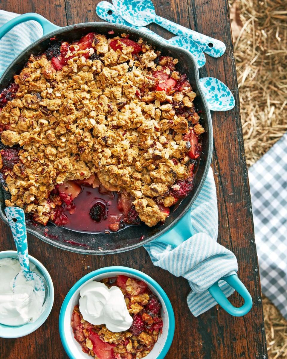 apple blackberry crumble in a cast iron pan with a bowl of sour cream whip on the side and speckled enamel spoons