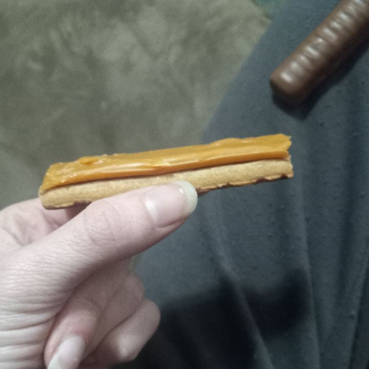 Person holding a caramel biscuit, with another chocolate-covered biscuit in the background