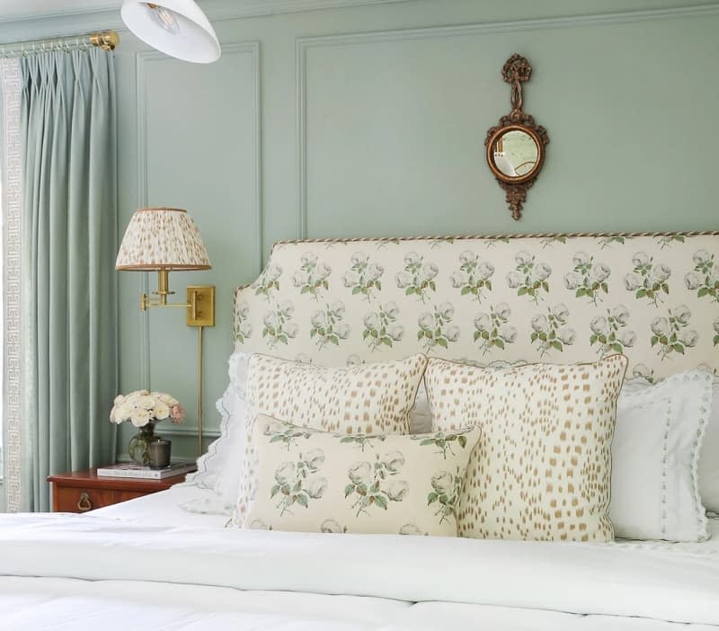 Throw pillows on bed with fabric headboard in sage bedroom with matching curtains.