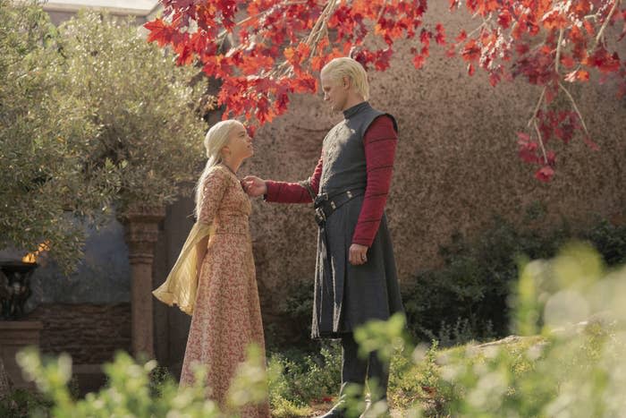 a man and a woman looking at each other by some trees