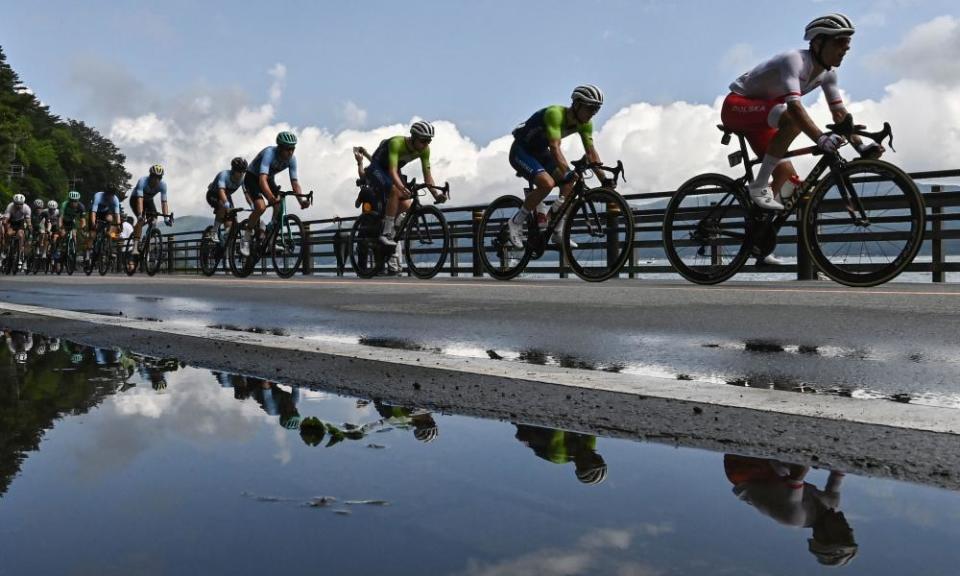 Cyclists in the peloton are reflected on a puddle as they ride past Yamanaka Lake.