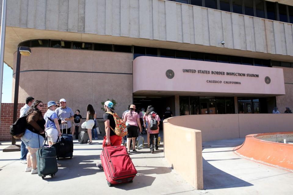 People with luggage walk toward a building.