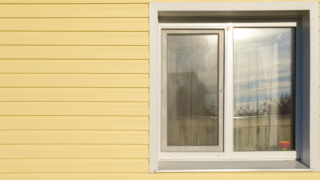 white plastic window on the wall lined with yellow siding.