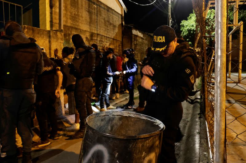 A police officer inspects a garbage barrel as other officers frisk men for drugs and weapons during the "Costa Rica Segura' operation, in San Jose