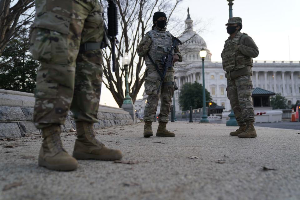 Armed men in camouflage stand with the Capitol dome in the background.